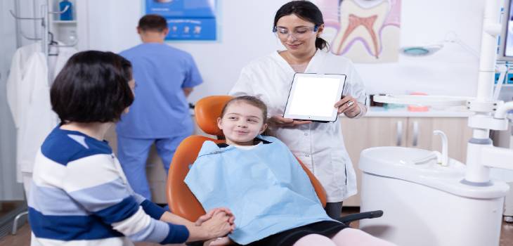 Kid wearing dental bib and doctor discussing with parent about cavity treatment