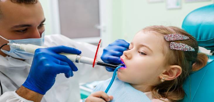 A professional doctor, a children's dentist, treats a little girl's teeth with instruments. Dental office for patient examination. The process of dental treatment in a child