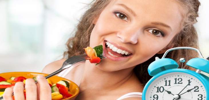 Retro alarm clock in which woman make intermittent fasting with a healthy food of salad