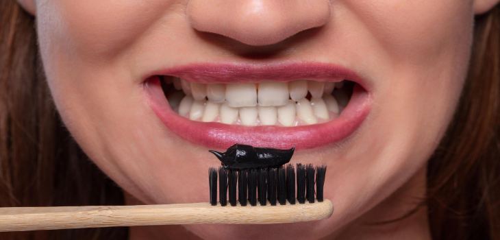 Woman holding tooth brush with black active charcoal toothpaste