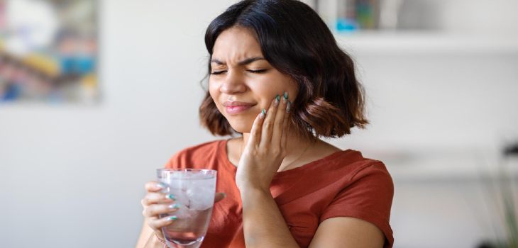 Sensitive teeth or teeth sensitivity and touching cheek with grimace of pain young arab woman and drinking water with ice